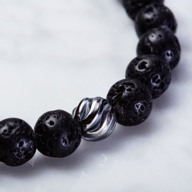 close up of Black lava 8mm beads has smooth surface but dotted by countless tiny holes. Has one accent sterling silver wave bead.